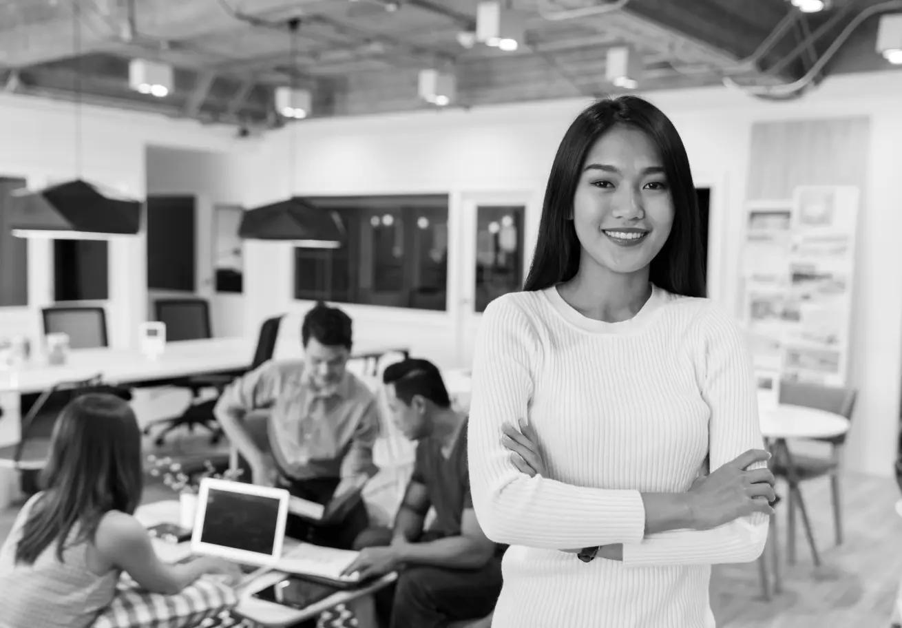 woman standing and smiling to the camera with her coworkers in the background
